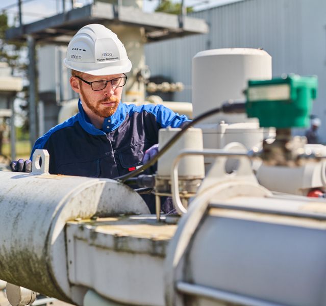 Ein Mann mit einem Schutzhelm und Brille arbeitet an einer technischen Vorrichtung arbeitet